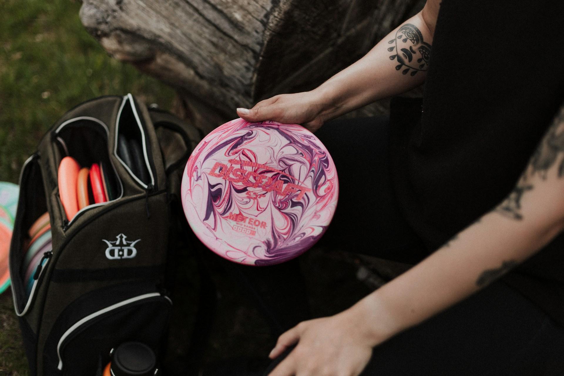 Spiller holder en rosa midrange ved discgolfbagen